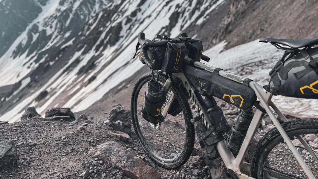 What Is Bikepacking? – Lighting, Gear, and Setup for Remote Exploration Close-up of a Canyon bikepacking setup in a snowy alpine environment, with frame bags, handlebar packs, and lighting gear prepared for extreme terrain and long-distance adventure.
